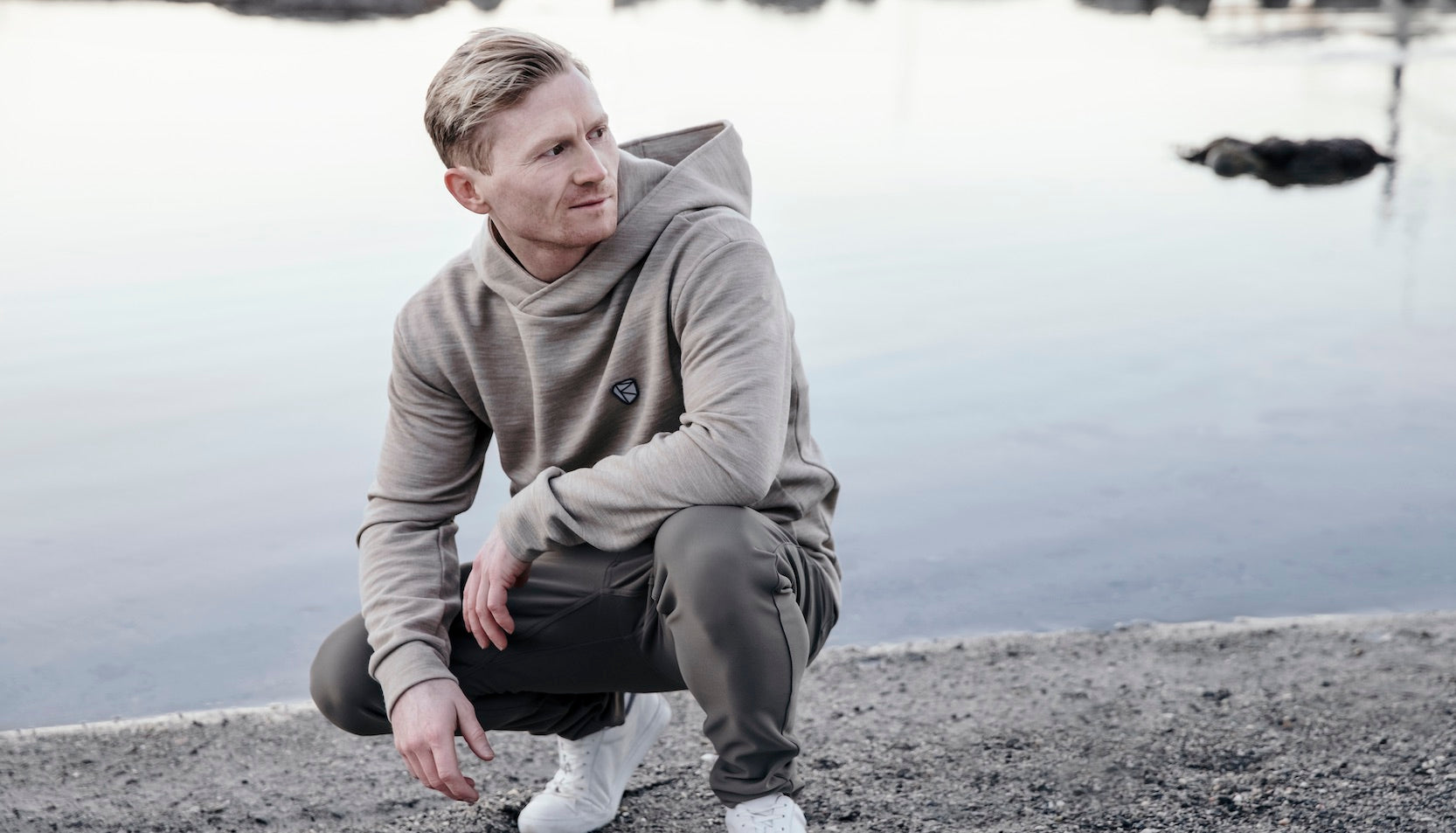 man crouching near the water in rungne pants