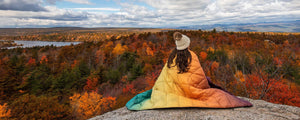 woman wearing rumpl puffy blanket on a ridge overlooking a forest