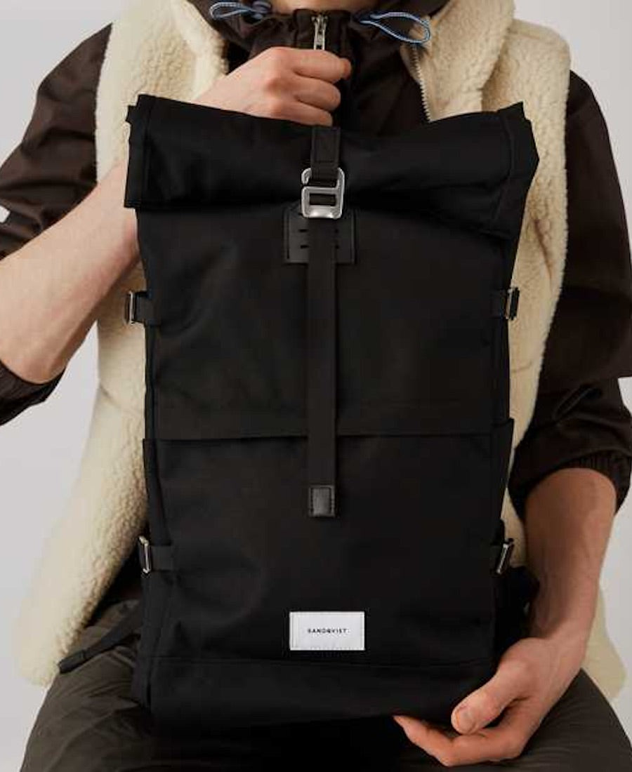 A guy holding a black rolltop backpack by Sandqvist of Sweden